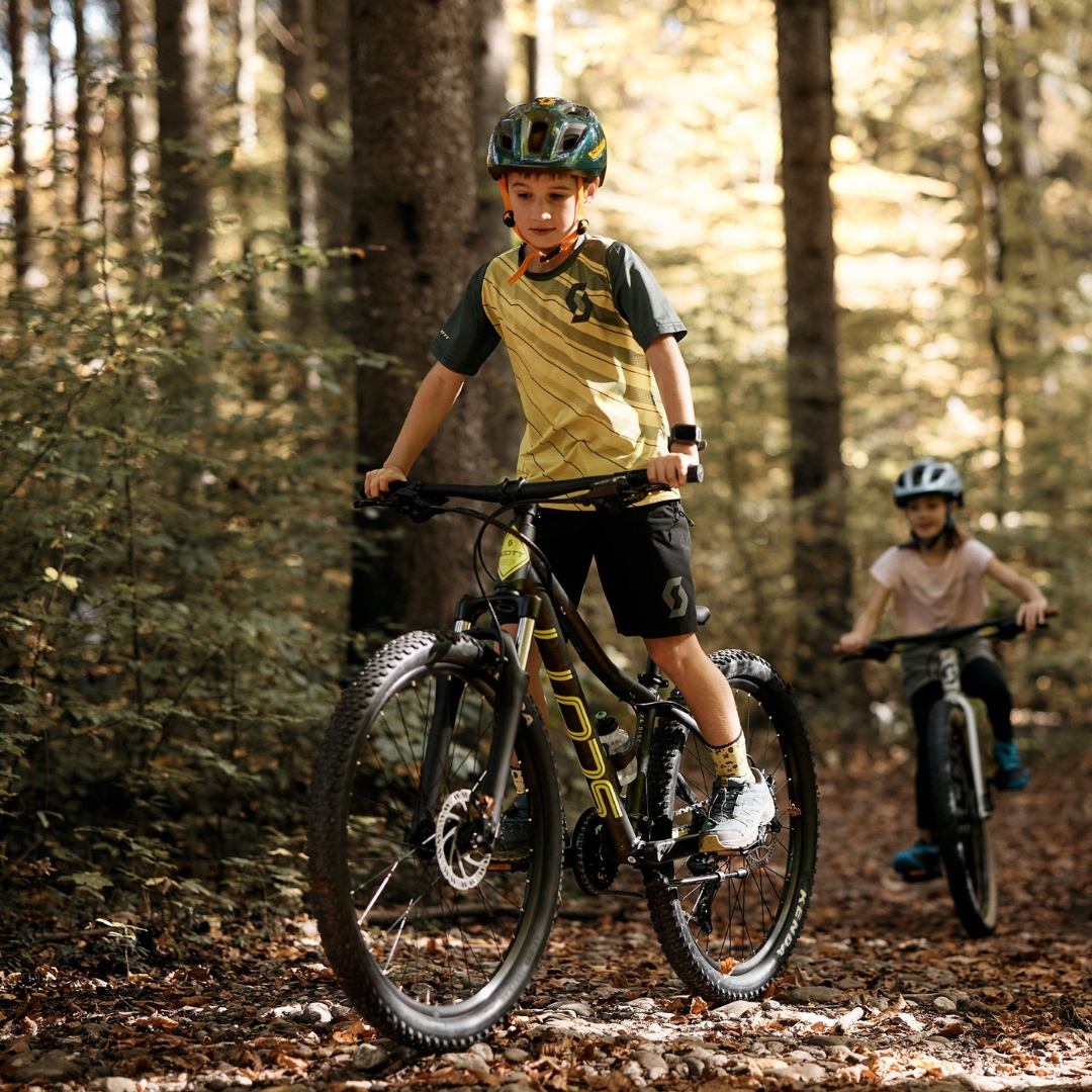 VÉLO DE MONTAGNE SCOTT ROXTER 26 DISC POUR ENFANT VU DU VÉLO NOIR utilisé par un jeune homme dans le bois