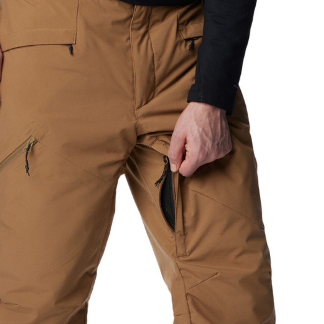 PANTALON DE NEIGE COLUMBIA KICK TURN III POUR HOMME couleur 257-DELTA vu du pantalon brun sable porté par un homme vu en gros plan sur le haut du pantalon l'homme montre l'ouverture à l'entrejambe