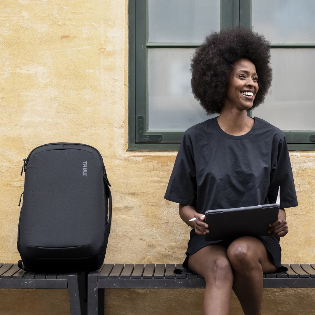BAGAGE DE CABINE CONVERTIBLE THULE SUBTERRA 2 une femme en ville assise à côté du sac sur un banc
