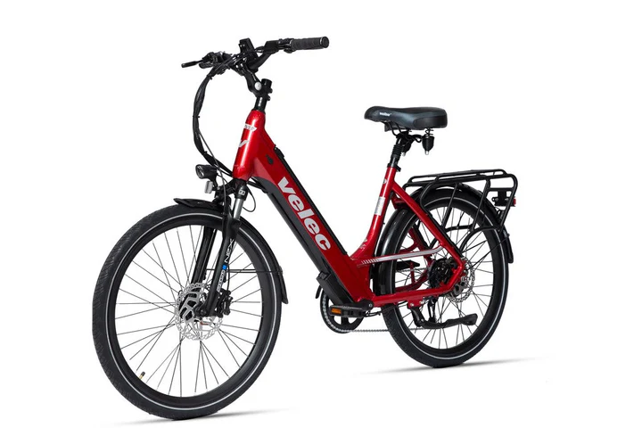 Vélo électrique rouge avec cadre à enjambement. Il est doté d'une suspension avant, de freins à disque et d'un porte-bagages arrière noir. Le nom de la marque « velec » est imprimé sur le cadre. Le vélo est présenté sur un fond blanc.
