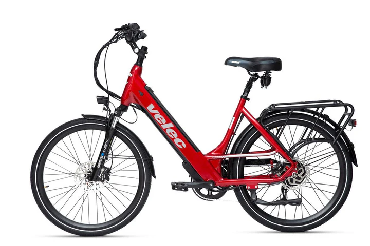 Vélo électrique rouge avec cadre à cadre ouvert et inscription « velec » sur le côté. Il est équipé d'une fourche à suspension avant noire, d'un guidon noir et d'un porte-bagages arrière. Le vélo est équipé de freins à disque et d'une selle noire confortable.