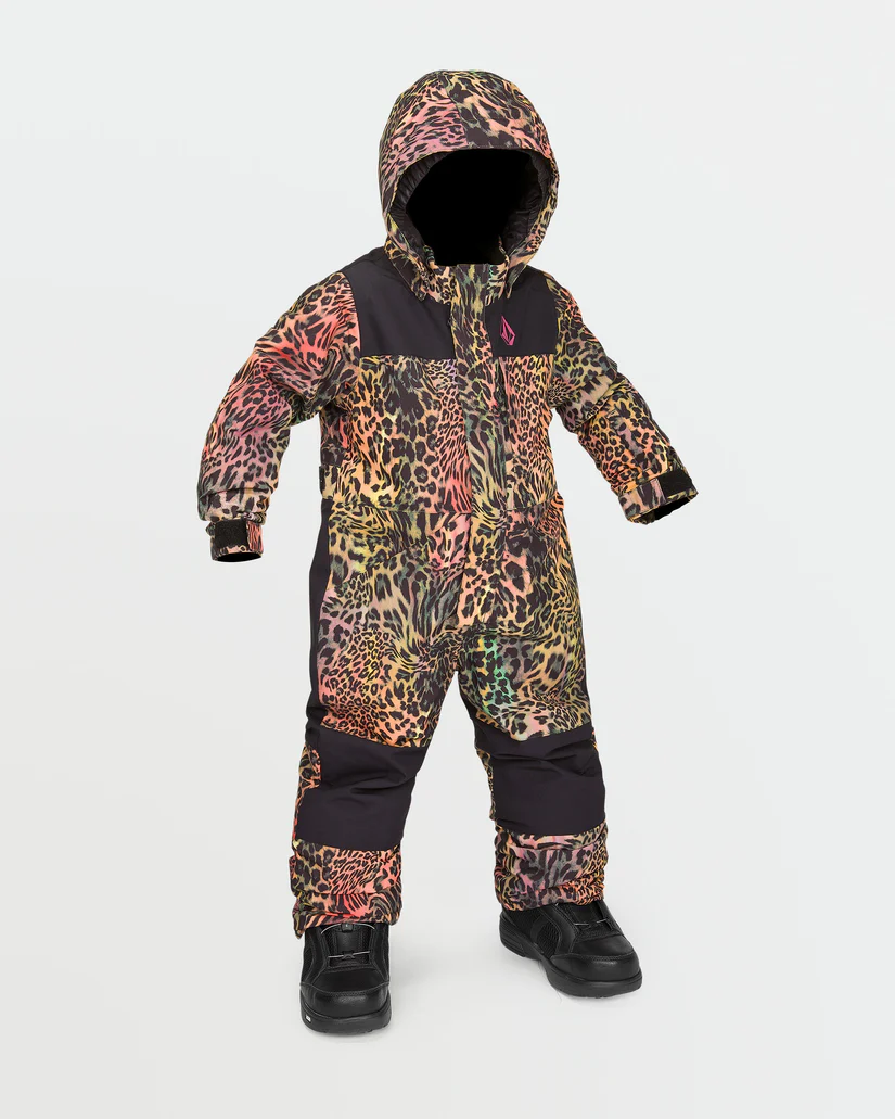 Un enfant porte une combinaison de neige à capuche avec un imprimé léopard multicolore vibrant. La combinaison de neige est composée d'un tissu principalement noir sur la poitrine et le bas des jambes avec des sections colorées sur les bras et le torse. L'enfant porte également des bottes noires.