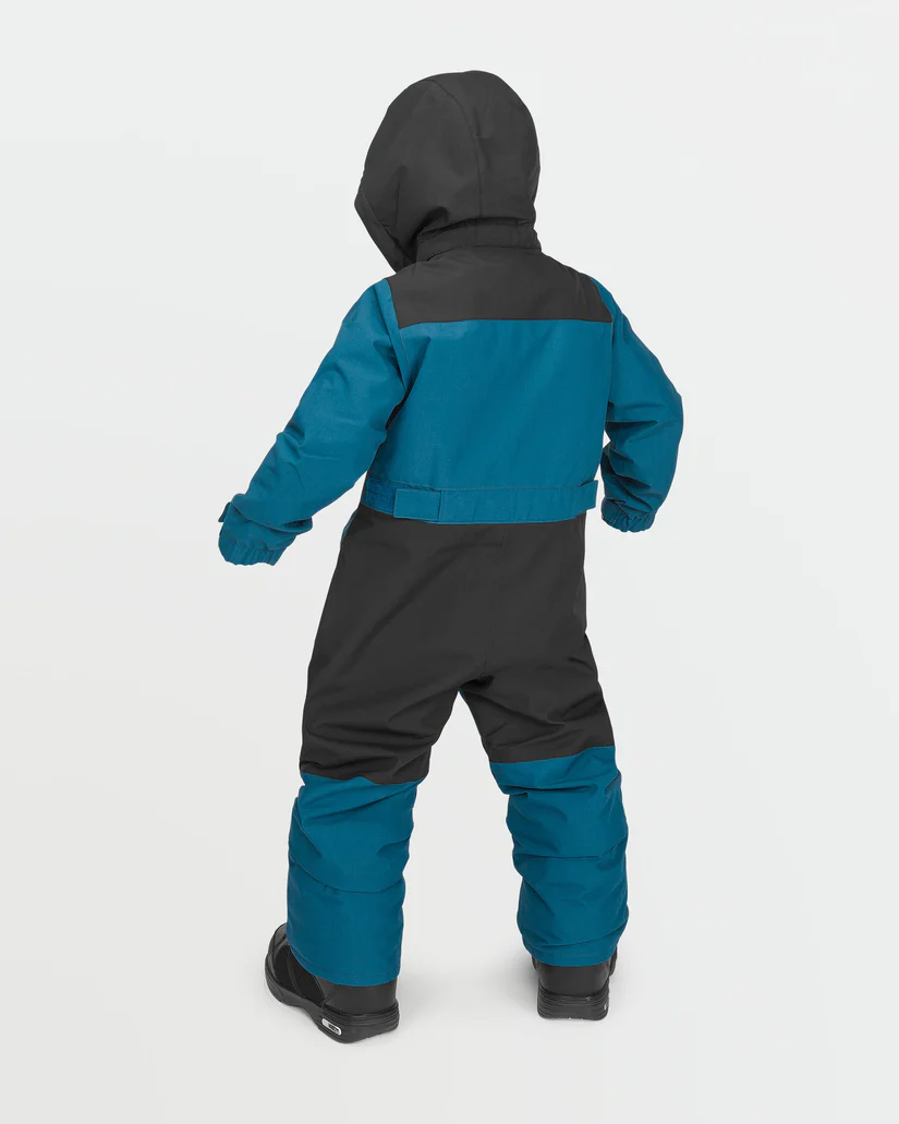 Un enfant porte une combinaison de neige à capuche bleue et noire avec des bottes noires, dos à la caméra. La combinaison a des poignets et des chevilles élastiques et un panneau noir sur le haut du dos. Le fond est blanc uni.