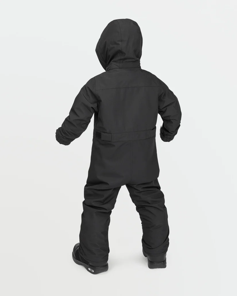 Un enfant, vu de dos, porte une combinaison de neige noire isolante avec capuche et poignets élastiques. L'enfant se tient debout sur un fond uni gris clair.