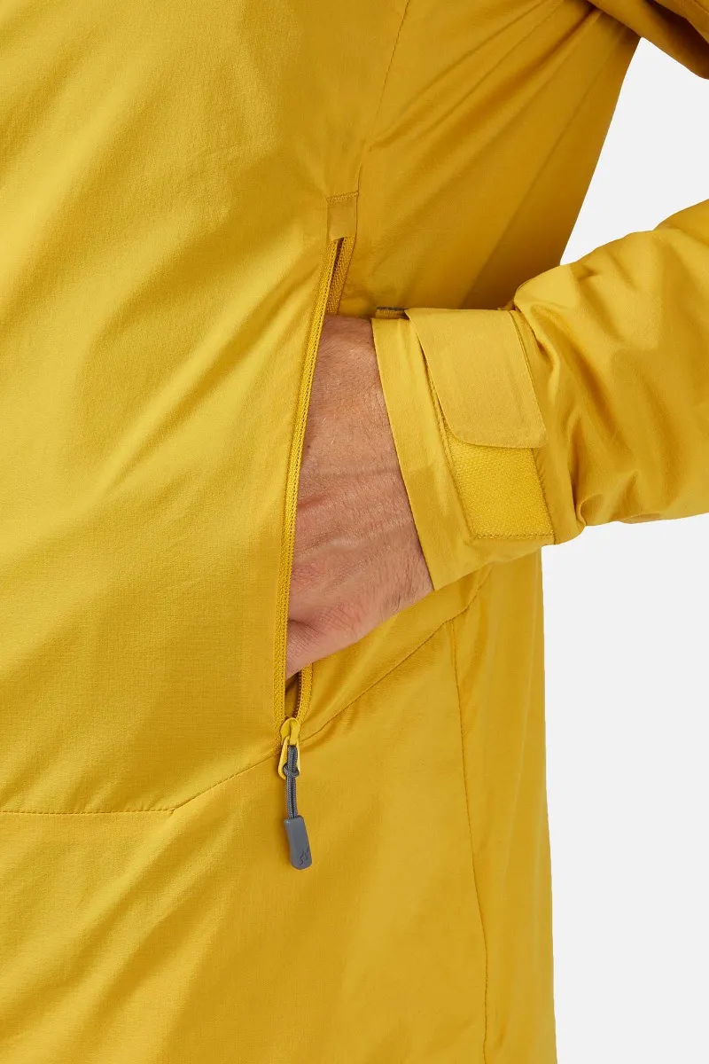 Personne portant une veste jaune avec une poche zippée, insérant sa main à l'intérieur. La manche de la veste est munie d'une bande Velcro. Le fond est blanc uni.