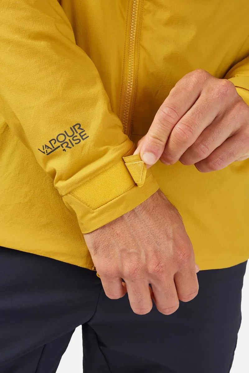 Une personne ajuste le revers d'une veste jaune avec une bande Velcro. Le mot « Vapor-Rise » est imprimé sur la manche. La veste est associée à un pantalon foncé.