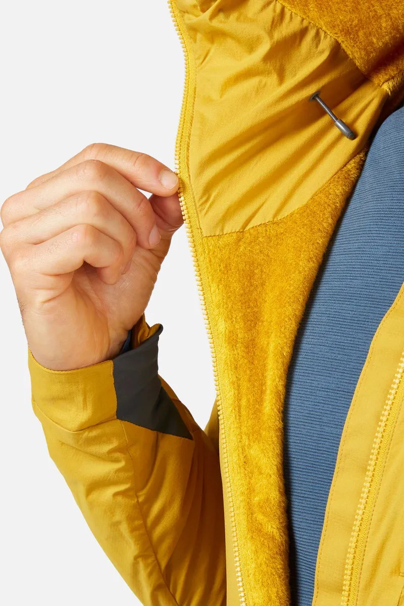 Une personne ferme la fermeture éclair d'une veste couleur moutarde avec une doublure en polaire. La main tient la tirette de la fermeture éclair, laissant apparaître une partie d'une chemise bleue en dessous.