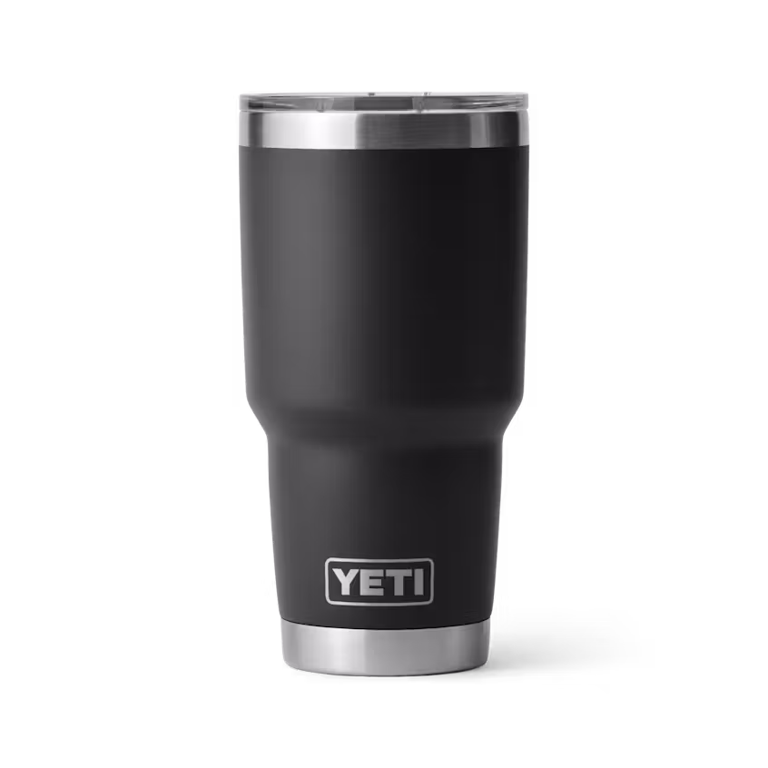 Un RAMBLER 30 OZ TUMBLER MS noir avec un bord et une base en acier inoxydable se tient debout sur un fond blanc, avec le logo YETI près du bas.